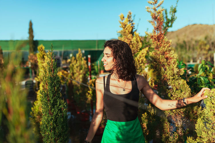 Smiling young woman standing by plants