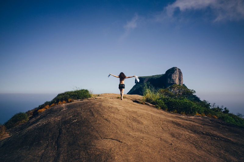Rear view of woman with arms outstretched walking on cliff