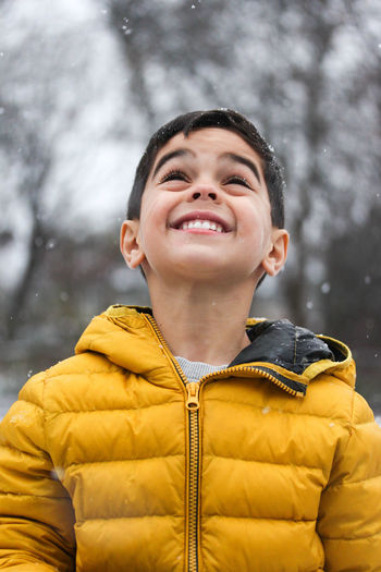 Low angle view of boy smiling standing outdoors during snowfall