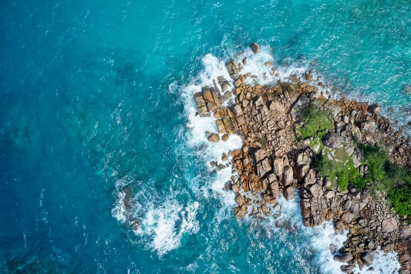 Drone field of view of waves crashing into rocky peninsula in praslin, seychelles.