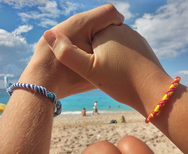 Close-up of couple holding hands on beach against sky