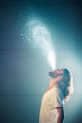 Close-up of bearded young man spraying water against wall