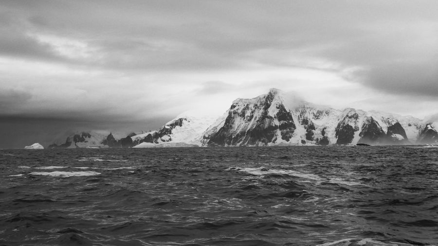 Black and white photo of sea against snowcapped mountain 