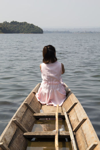 Rear view of young woman sitting on boat by sea against clear sky
