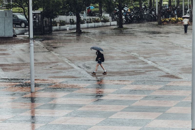 Woman with umbrella walking on wet footpath