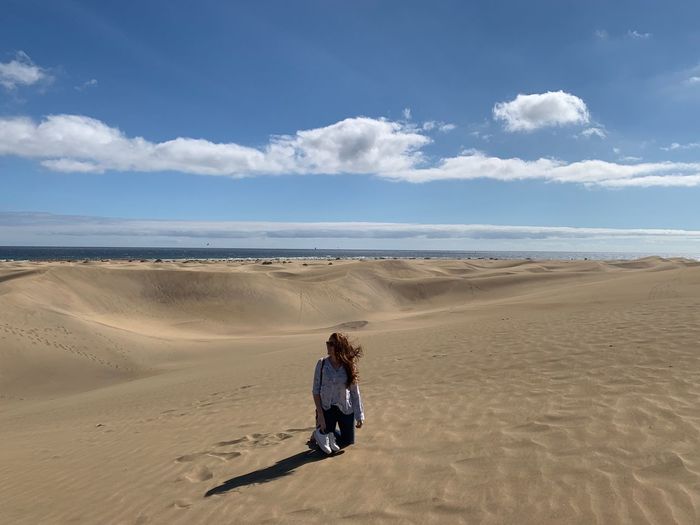Young woman kneeling in desert against sky