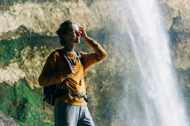 Portrait of an active woman hiker with a backpack in a mountain canyon near a large waterfall.