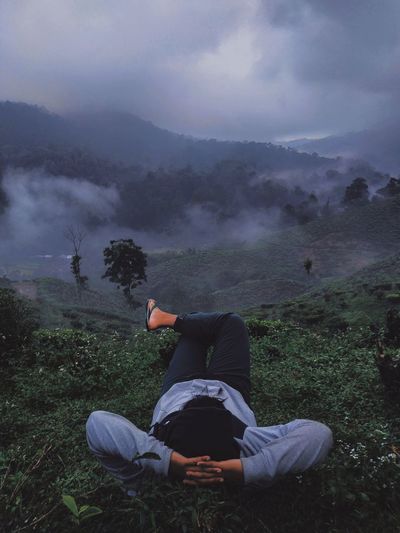 Man sitting on mountain against sky