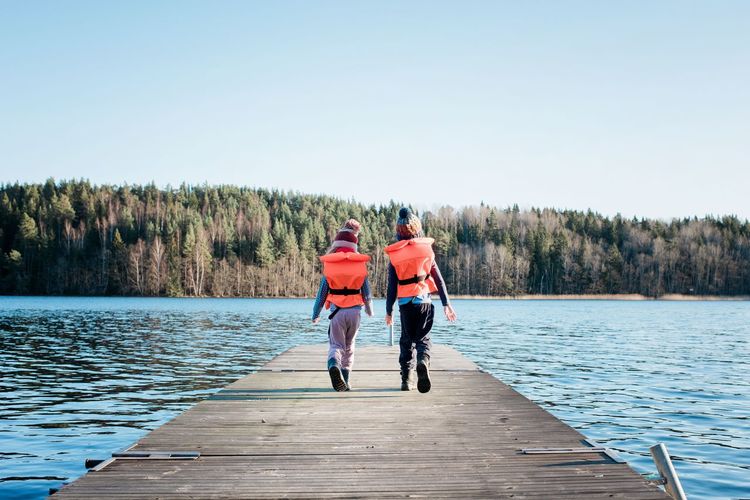 Brother and sister walking along a pier in winter with life vests on