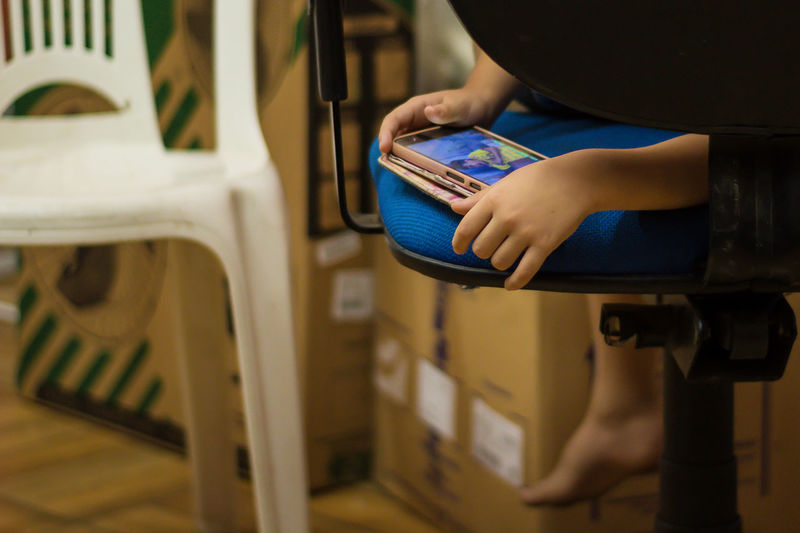 Low section of child using mobile phone on chair at home