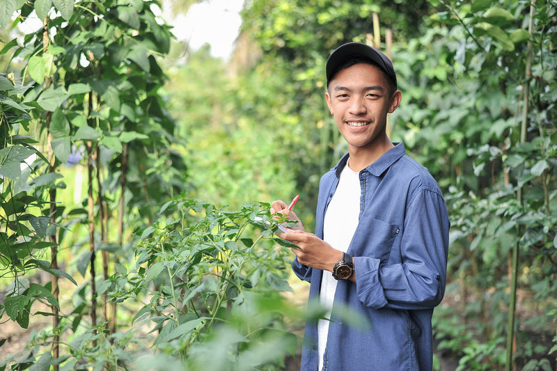 Happy of smiling young asian farmer male holding the notebook on green garden