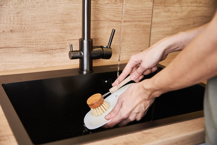 Woman washes dishes with wooden eco friendly brush. zero waste concept