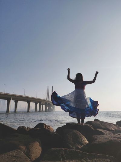 Rear view of woman on rock at beach against clear sky