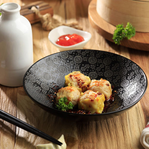 Mini chinese dim sum with chilli oil on a black bowl above wooden table