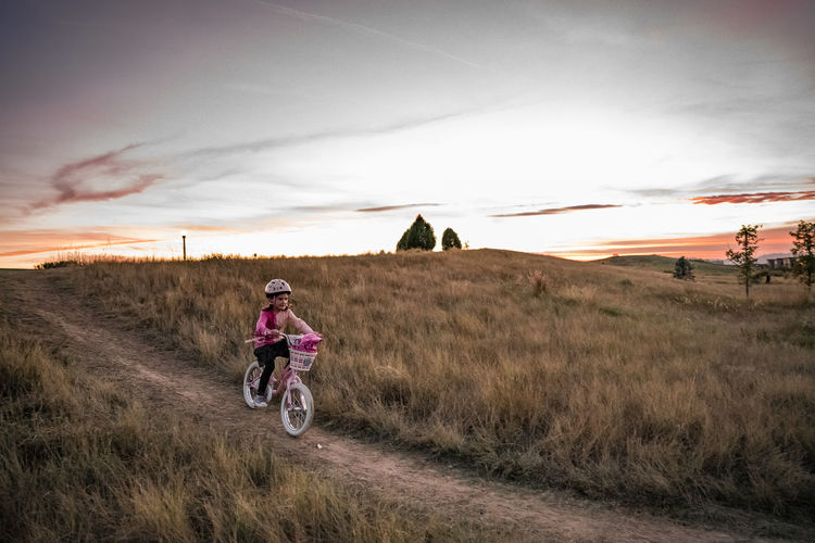 Young girl bikes down a grassy hill at sunset