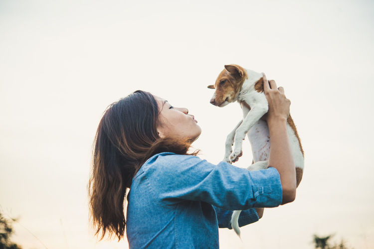 Low angle view of woman holding puppy against clear sky