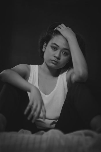 Portrait of a young woman sitting against black background