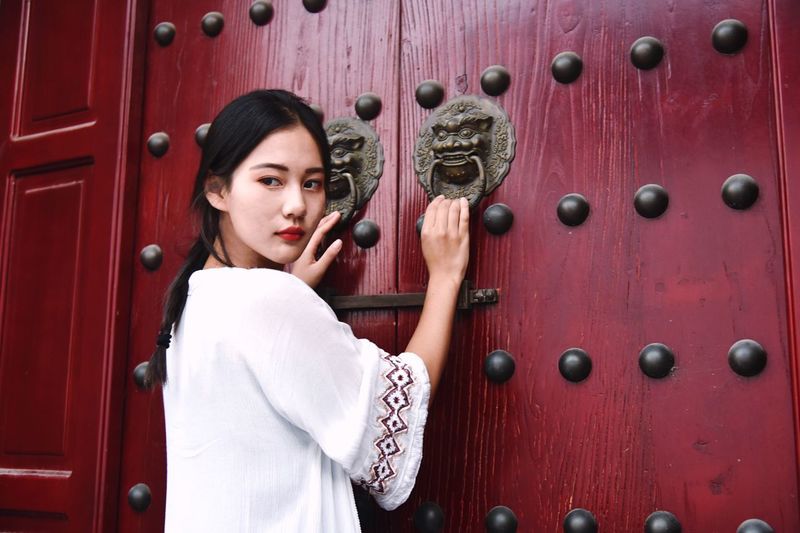 Young woman holding door knockers of maroon wooden gate