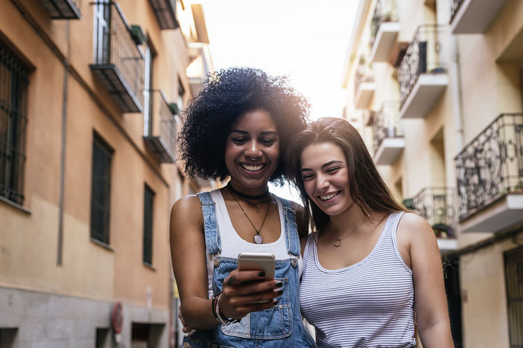 Female friends using phone in city