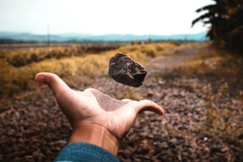 Cropped hand of man tossing stone on field