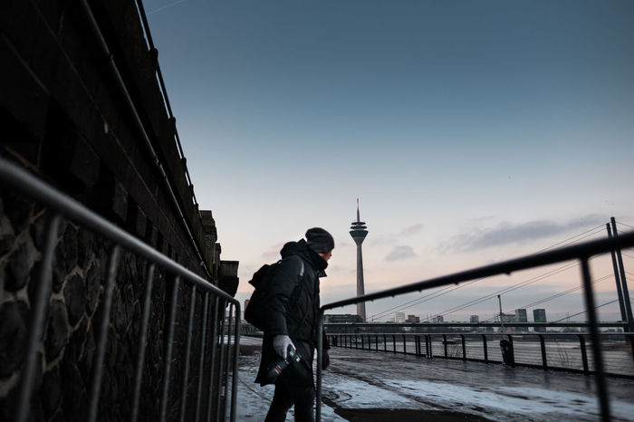 Man holding camera standing on promenade against rheinturm tower during winter