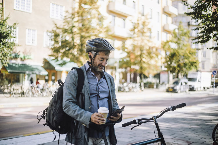 Mature businessman with disposable cup using smart phone by bicycle