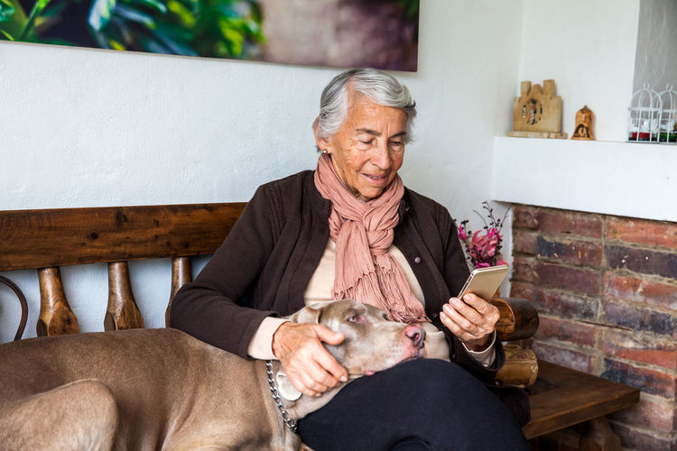 Senior woman using digital tablet with dog sitting on bench at home