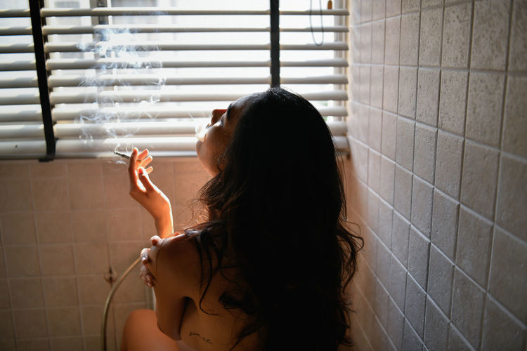 Seductive woman smoking cigarette in bathroom at home
