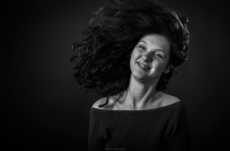 Smiling young woman tossing hair against black background