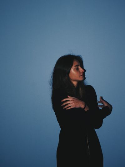 Side view of teenager girl hugging self while standing against blue background