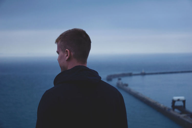 Rear view of man standing by sea against sky