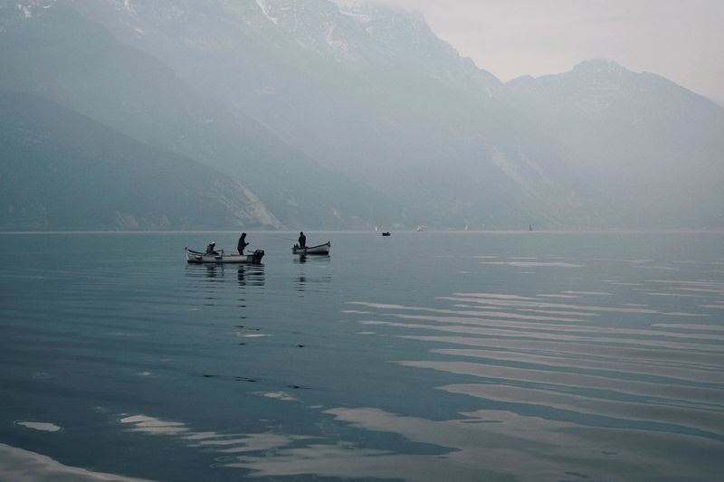 Boats sailing in river against mountains during foggy weather