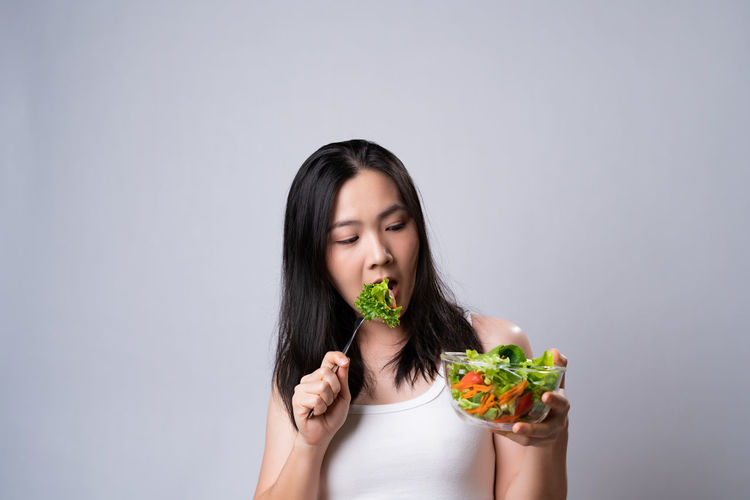 Portrait of woman eating food against white background