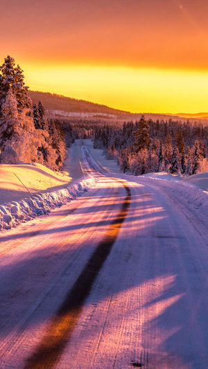 Road by snow covered landscape against orange sky
