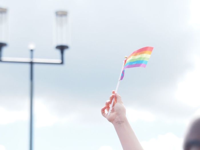 Midsection of person holding rainbow flag against sky