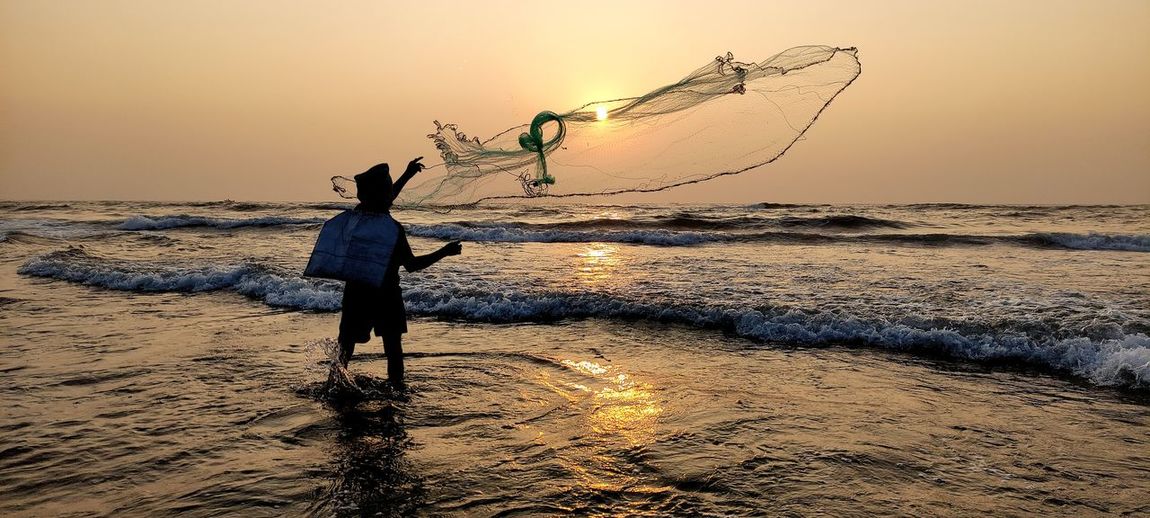 Full length of silhouette fisherman fishing on beach against sky during sunset