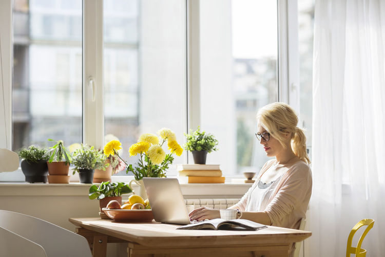 Woman using laptop computer while sitting by window at home