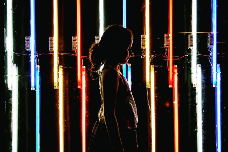 Side view of young girl against colored lights