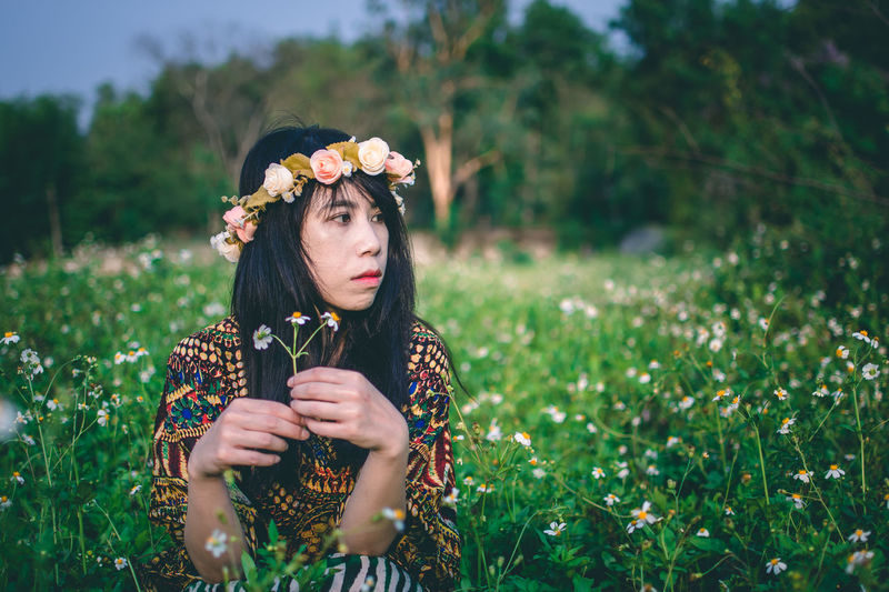 Woman wearing flowers while sitting on field 