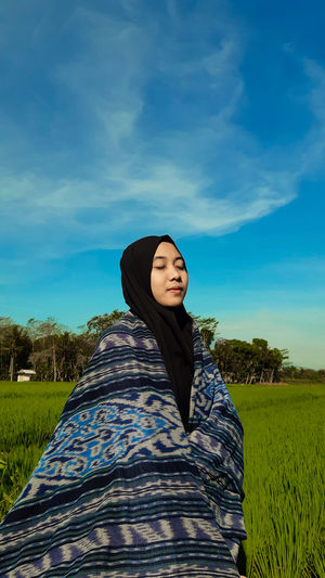 Smiling young woman with eyes closed standing on land against sky