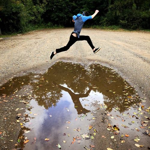 Man jumping over puddle on dirt road 