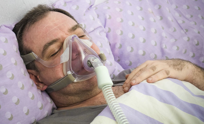 Close-up of man wearing oxygen mask while sleeping on bed at home