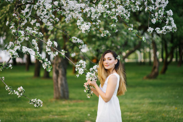 Portrait of a young beautiful woman in the spring flowers of an apple tree