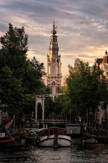 Boats moored on canal against church in city during sunset