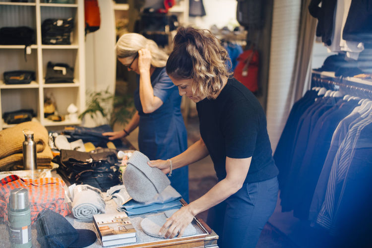 Female coworkers arranging clothes in retail store