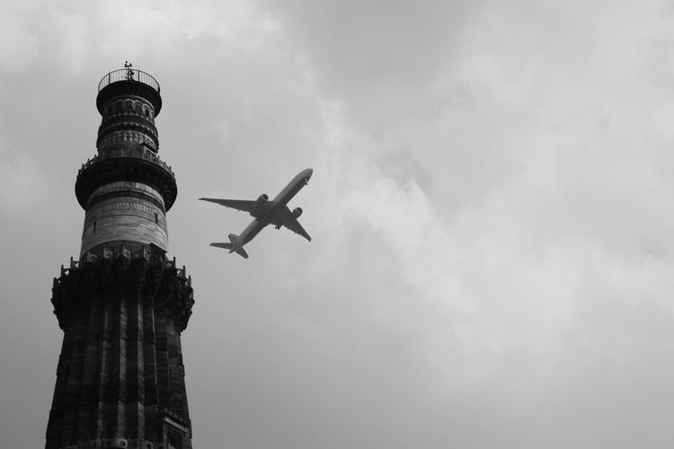 Low angle view of qutub minar against airplane flying in sky