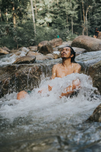 Shirtless man sitting on stream in forest