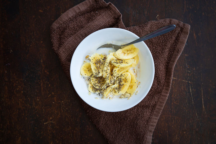 Cereal bowl with slice bananas sprinkled with chia seeds in a bowl on a dark background.