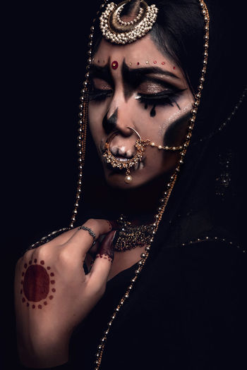 Close-up of young woman in traditional clothing with spooky make-up against black background