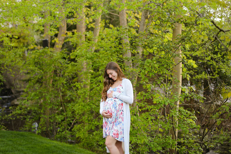 Smiling pregnant woman standing against trees